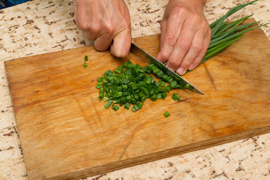 Chef chopping a green onion with a knife on the cutting board