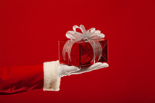Photo of Santa Claus gloved hand with  giftbox, on a red