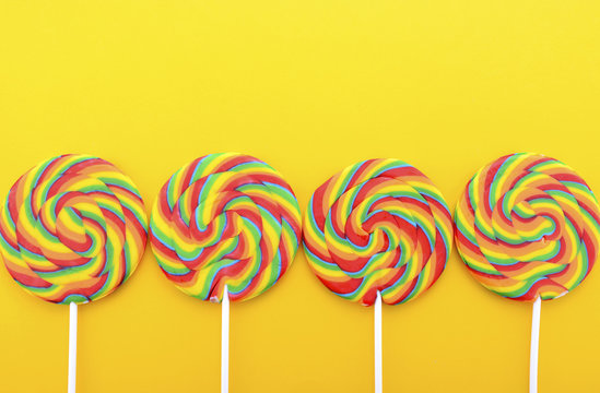 Rainbow lollipop candy on bright yellow wood table.