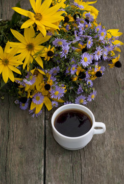 bouquet of wild flowers and cup of coffee on a wooden table, the
