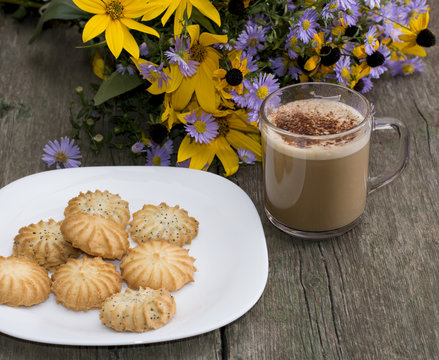 plate with cookies, a mug of a cappuccino and a bouquet of wild