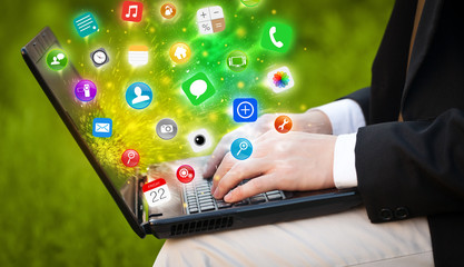 Hand pressing modern laptop with mobile app icons and symbols