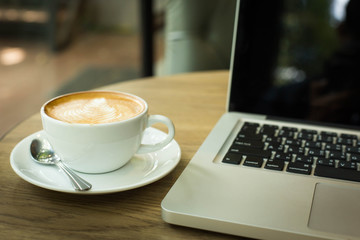 Hot art Latte Coffee in a cup on wooden table and and laptop in