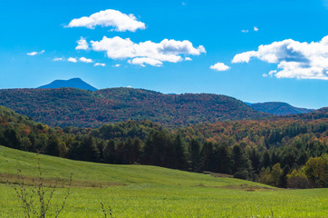 Fototapeta na wymiar meadows and fields with hills in fall foliage color and Camels Hump against the sky 