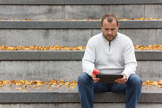Tablet PC / A man sitting with a tablet PC a gray stone staircase with yellow autumn leaves