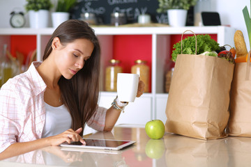 Woman using a tablet computer while drinking tea in her kitchen