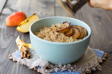 Oatmeal with baked apples and cinnamon in blue ceramic bowl on wooden table 