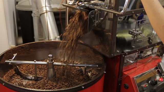 Coffee Bean Pour. The camera dollies from right to left as roasted coffee beans pour out into the industrial sifter.
