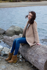 stylish girl in autumn coat sitting by the water