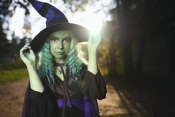 Young girl with green hair and skin suit of witch in forest. Halloween time