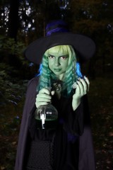 Young girl with green hair and flask with a potion in suit of witch in forest. Halloween time