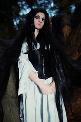 Young beautiful witch with long dark hair in root of old tree