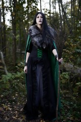 Young beautiful girl in green raincoat, looks as witch on Halloween in forest