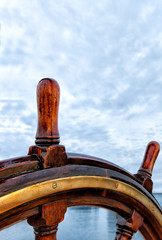 Ship wheel made of wood and brass on a sailboat at sea. Close up with copy space. Concept for...
