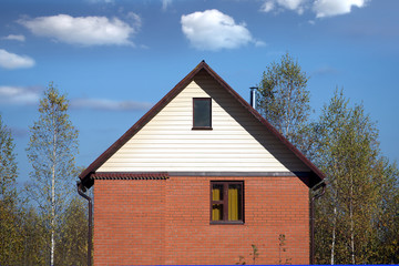 Obraz premium Front view of a new country house from red brick, brown roof covered and siding on the top and a metal chimney near forest