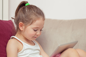 Fototapeta premium cute little girl playing with tablet computer at home