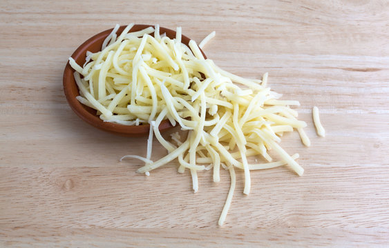 Portion of natural white mild cheddar cheese spilling from bowl