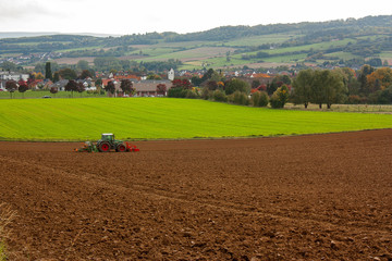 An agricultural landscape with a tractor plowing the soil.