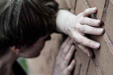 A woman in a very depressed mood stands near the brick wall.
