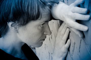 A woman in a very depressed mood stands near the brick wall.
