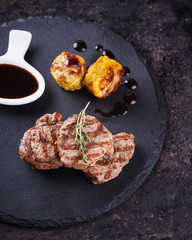 Pieces of red meat, steaks with vegetable and spices, served on black stone surface. selective focus