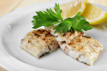 Dish of fish fillet with greens and lemon on plate close up