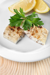 Dish of fish fillet with greens and lemon on plate close up
