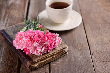 Naklejka na ściany i meble Old book with beautiful flowers and cup of tea on wooden table close up