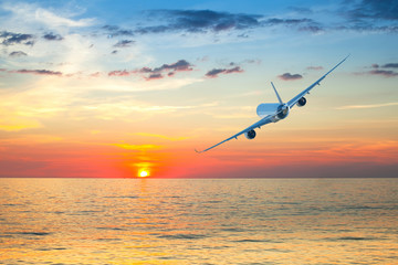Jumbo jet airplane flying above tropical sea at beautiful sunset.