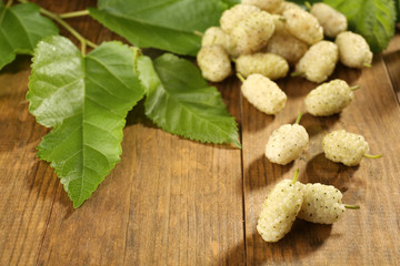 Heap of ripe mulberries with green leaves on table close up