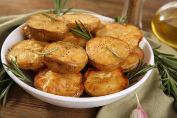 Delicious baked potato with rosemary in bowl on table close up
