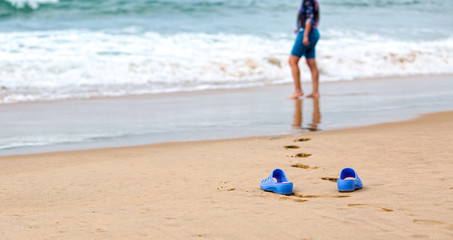 Beach Slippers and Blurred Silhouette of a Woman in Waves