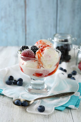 Delicious ice cream with fresh frozen berries and sauce, on color wooden background