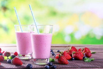 Glasses of berry smoothie on wooden table on blurred background