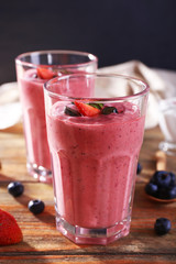 Glasses of berry smoothie on wooden table on dark background