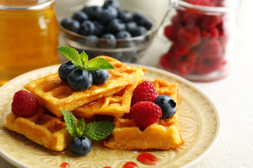 Sweet homemade waffles with forest berries and sauce on table background