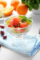 Fruit salad in glass bowl, on light wooden background