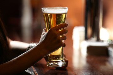 Woman holding beer glass, close-up, on bar interior background