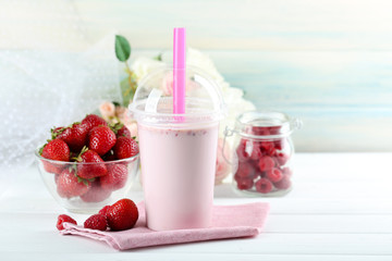 Plastic cup of milkshake on light wooden background