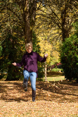 Woman enjoying the fall leaves, walking through the leaves and kicking them up
