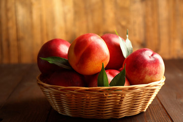 Fresh peaches in wicker basket on wooden background