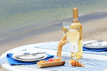 Obraz premium Romantic beachside dining experience with white wine, starfish, and seashells on a striped tablecloth by the ocean