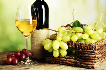 Bunch of white grape in basket with wine bottle on wooden table