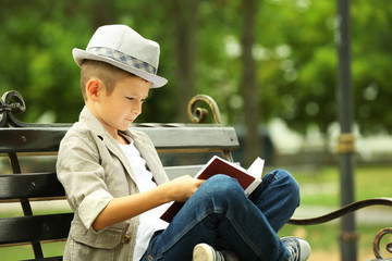 Obraz na płótnie Canvas Little boy reading book on bench in the park