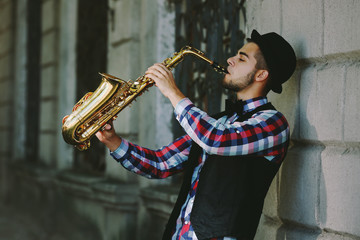 Man with saxophone outside near the brick wall