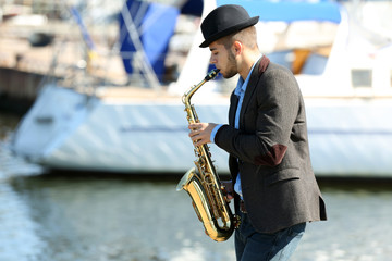 Young man playing on saxophone on the riverside