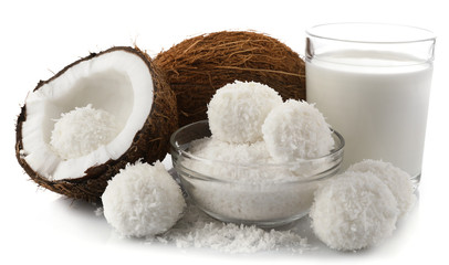 Candies in coconut flakes, glass of milk and fresh coconut isolated on white