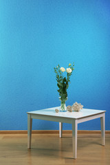 Little table with flowers on blue wall background