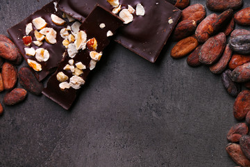 Black chocolate pieces with nuts and cocoa beans on dark gray background