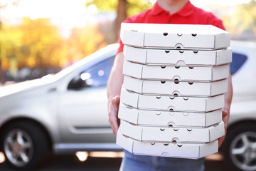 Livreur de pizza tenant des boîtes avec pizza près de la voiture